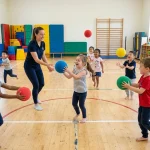 Děti a paní učitelka při zábavných míčových hrách v tělocvičně školky