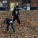 Předškolní děti v teplých bundách házející spadané barevné listí na podzimní zahradě
